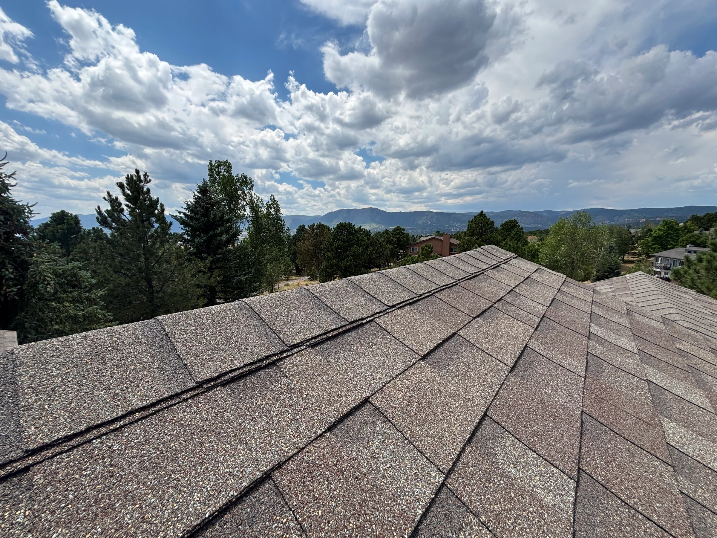 Shingle roof ridge with trees and mountains beyond in Colorado Springs